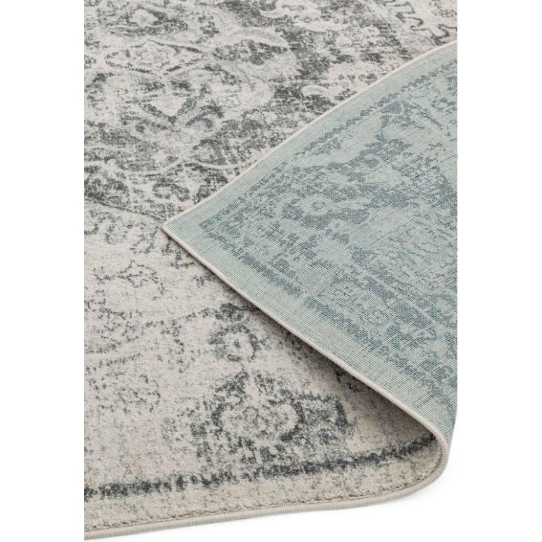 Grey and cream patterned area rug with corner lifted to show woven backing