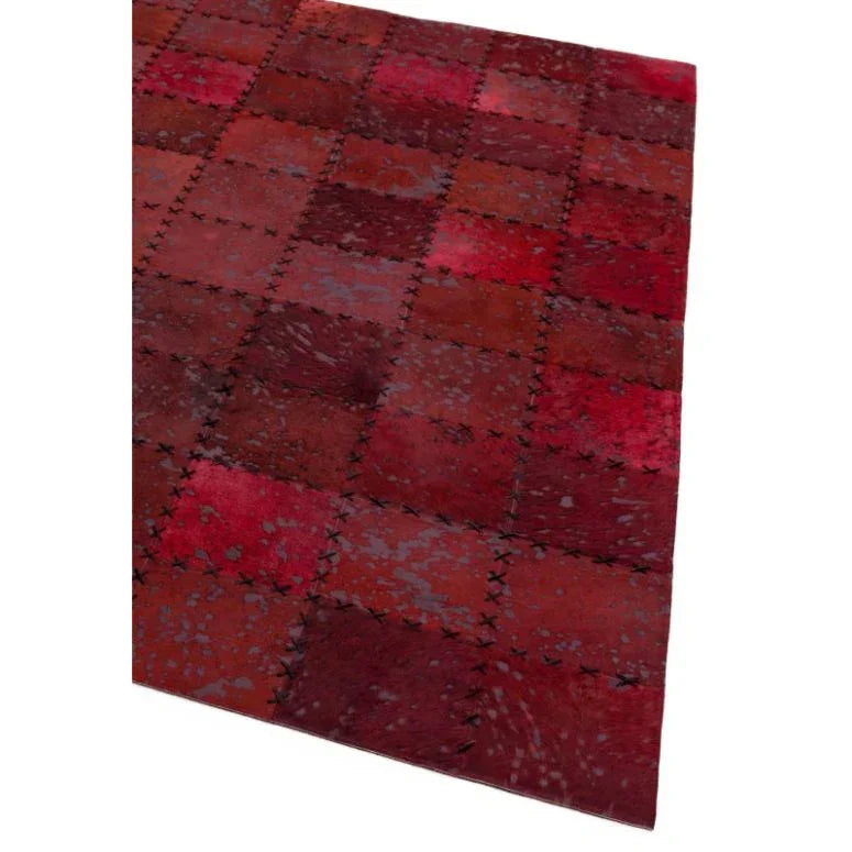 Red patchwork cowhide rug with visible stitched square pattern, angled corner view