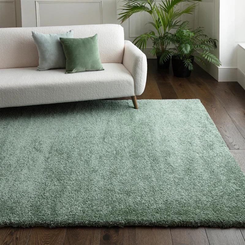 Sage green shaggy rug on dark wood floor beside cream sofa with green cushions