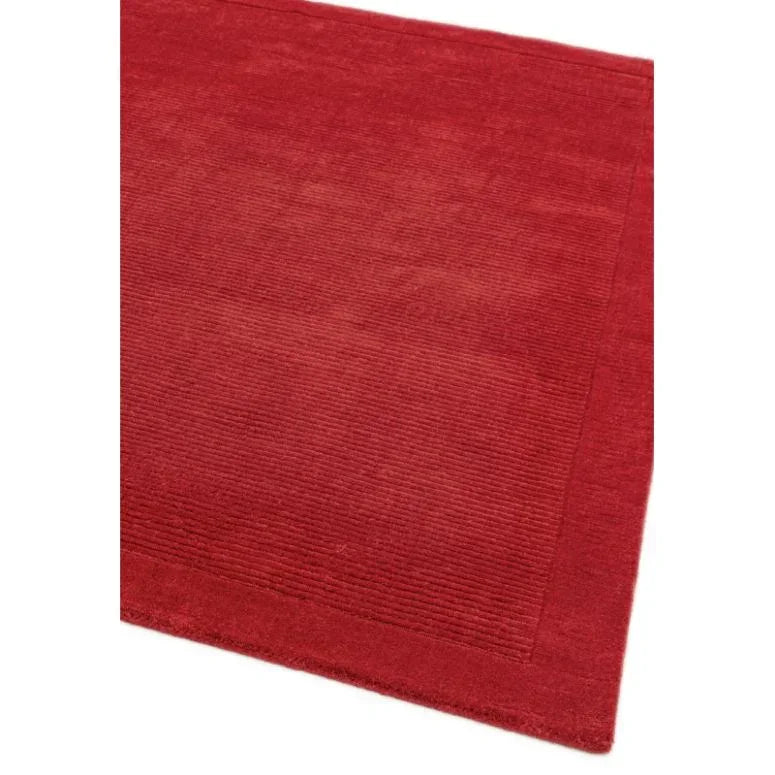 Red wool rug with ribbed border texture, shown from angled corner view