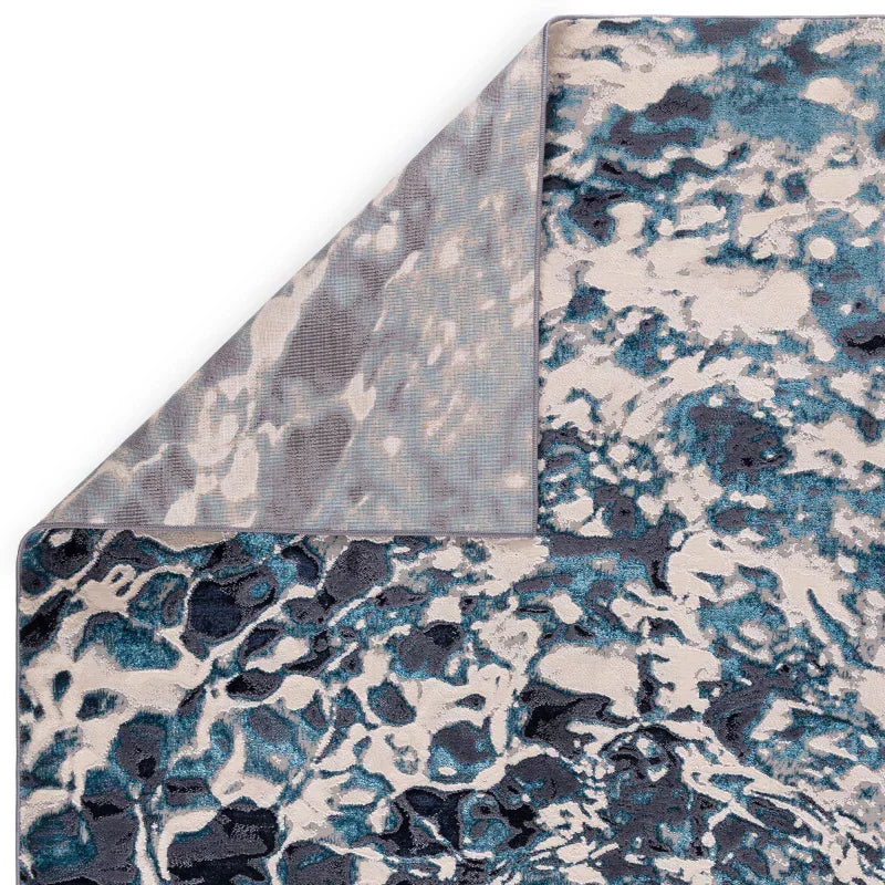 Blue and grey abstract patterned rug with corner folded to show backing