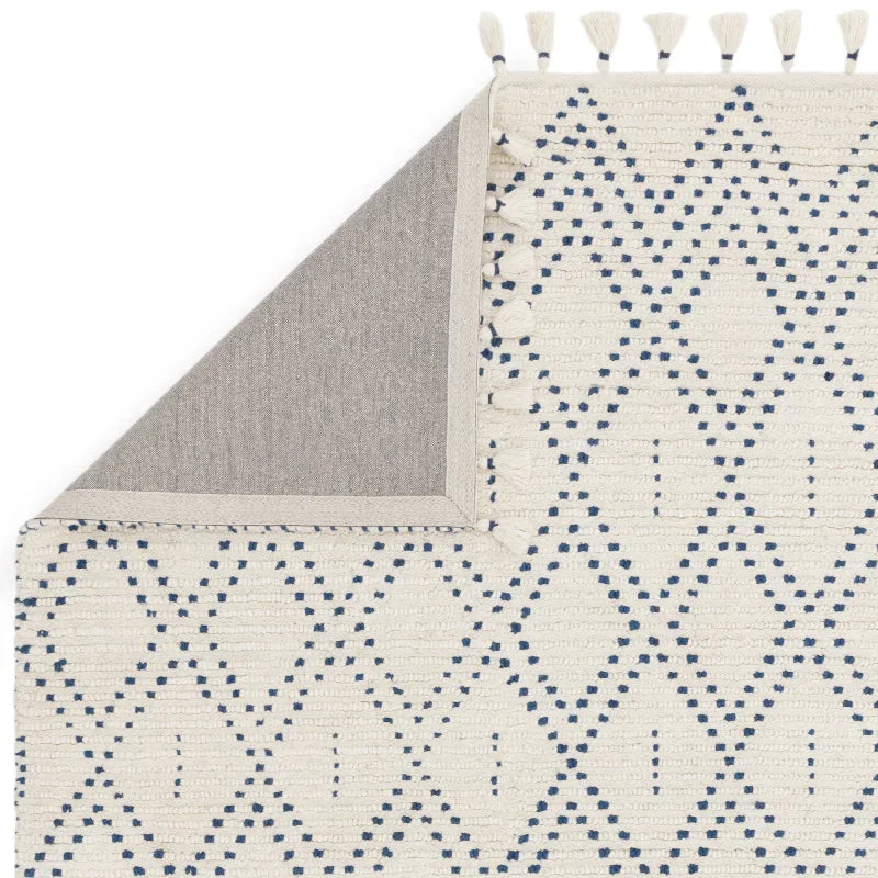 Cream and blue patterned area rug with fringe and corner folded to show backing