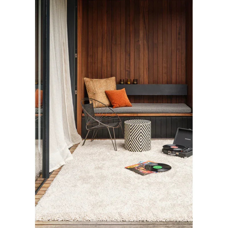 Shaggy cream rug in modern wood room with bench, accent chair, pouffe, and record player