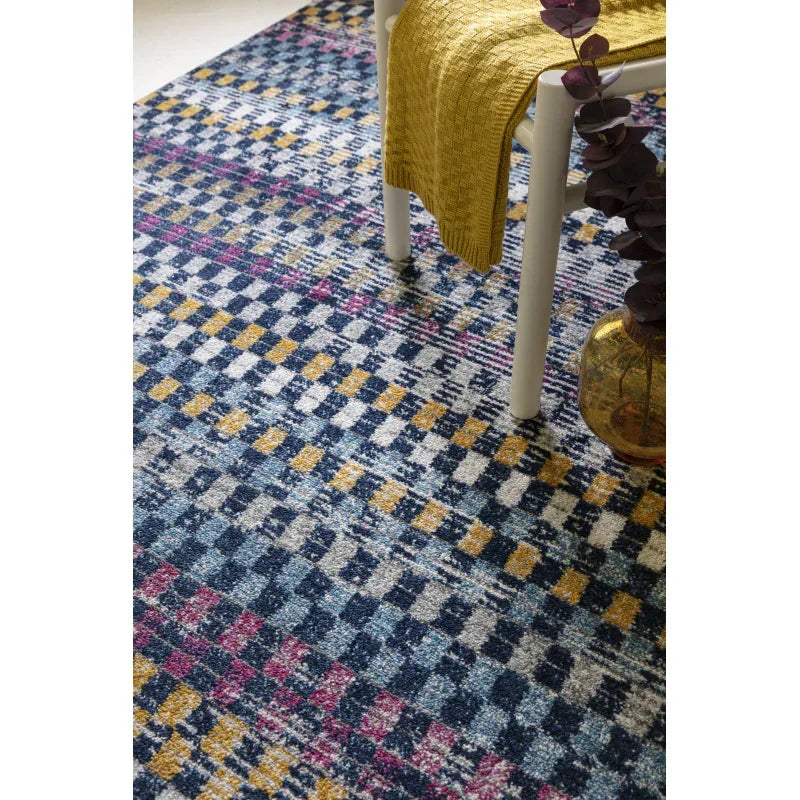 Checkered area rug with blue, yellow, and pink pattern under a chair with a yellow throw