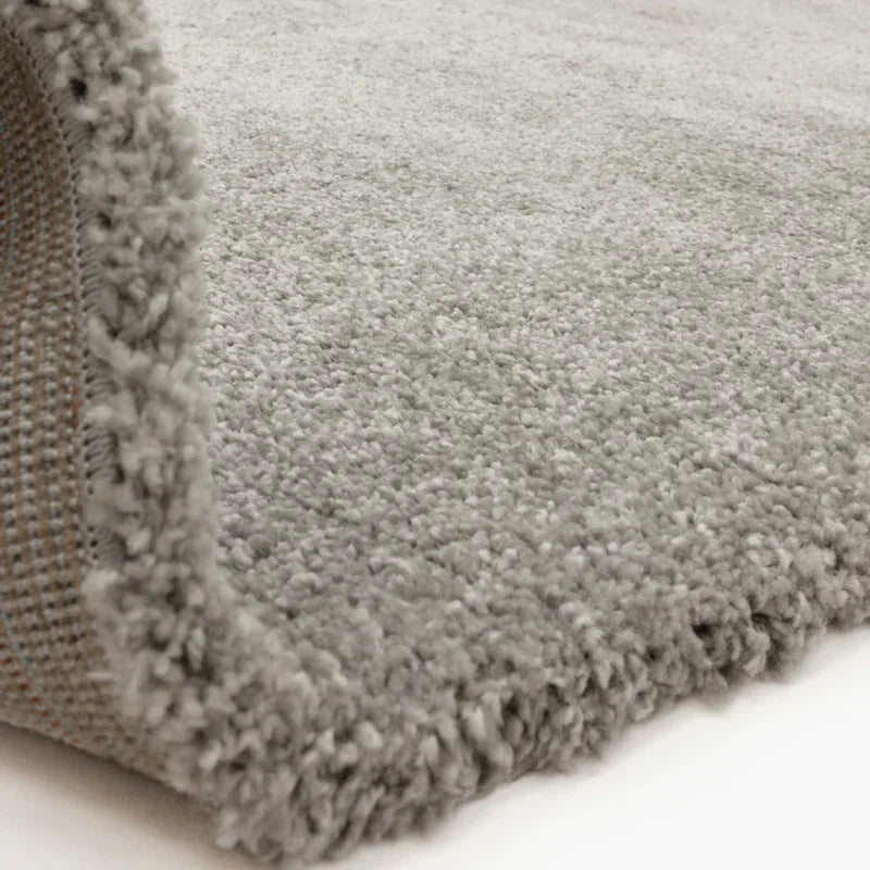 Close up of light grey shaggy rug with soft pile and visible woven backing