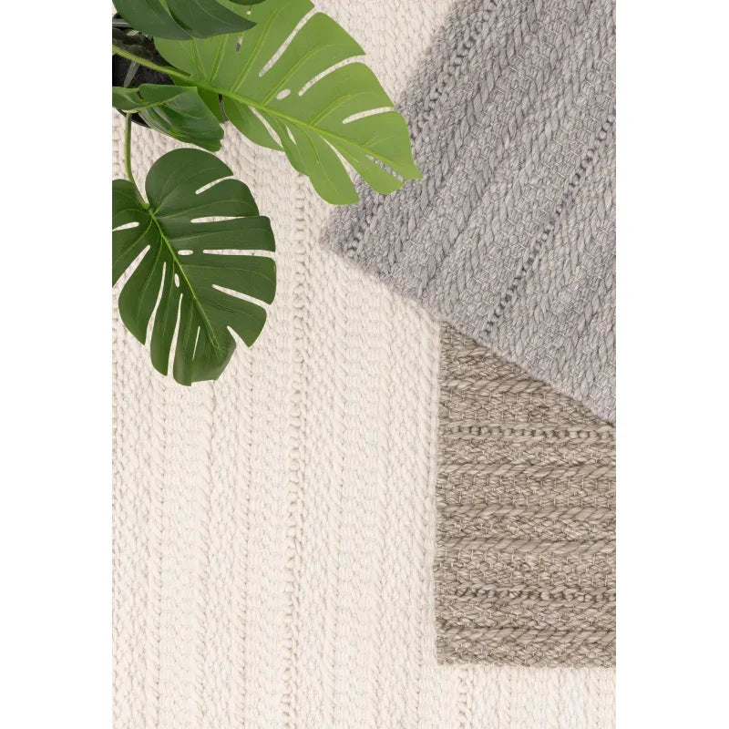 Textured woven rugs in cream, grey, and taupe with green monstera leaf decor