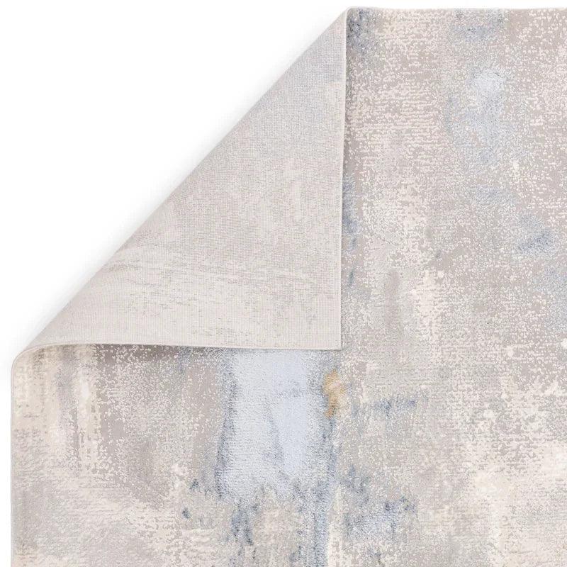 Abstract area rug in grey and blue tones with corner flipped to show backing
