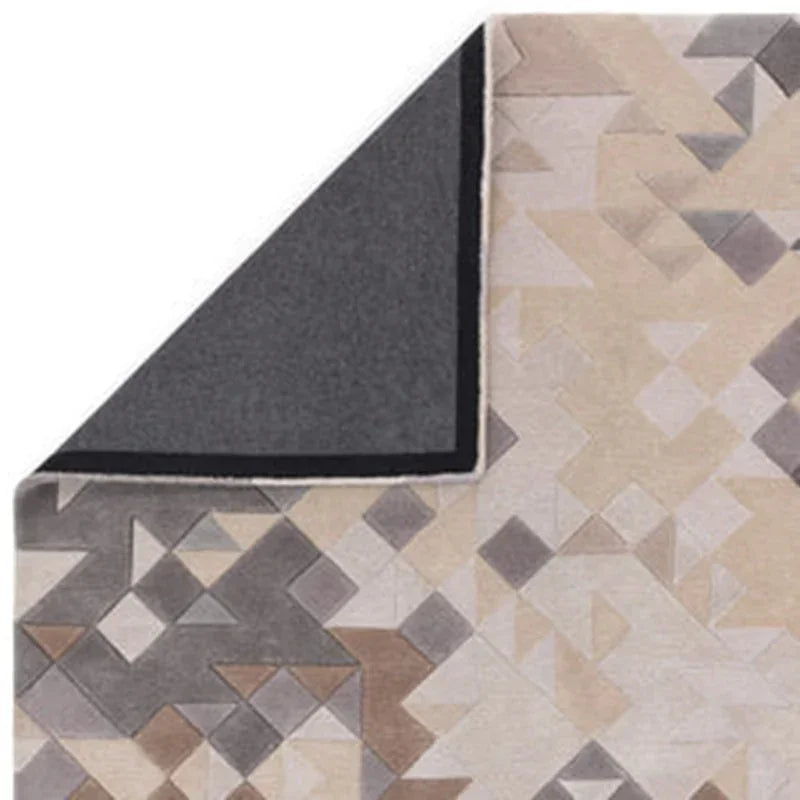 Geometric patterned area rug in beige, grey, and taupe with visible corner fold