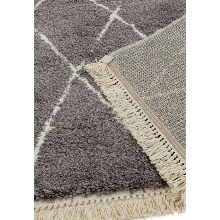 Grey shaggy rug with white diamond pattern and cream fringe detail, close view