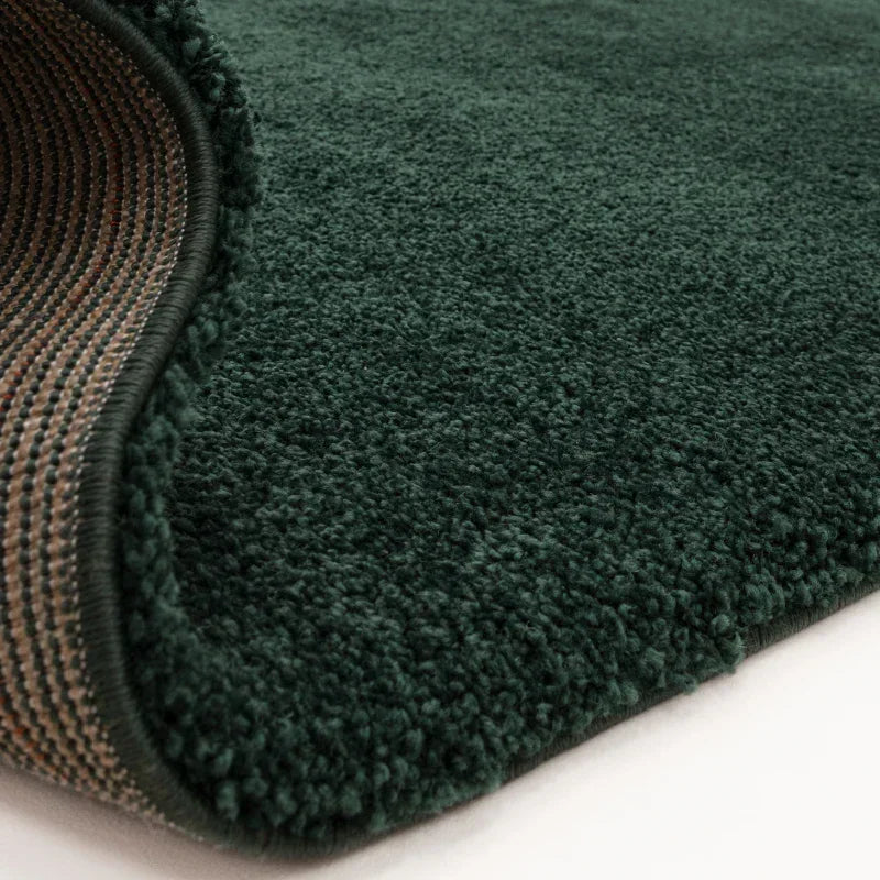 Close-up of dark green pile rug with soft texture and detailed edge stitching