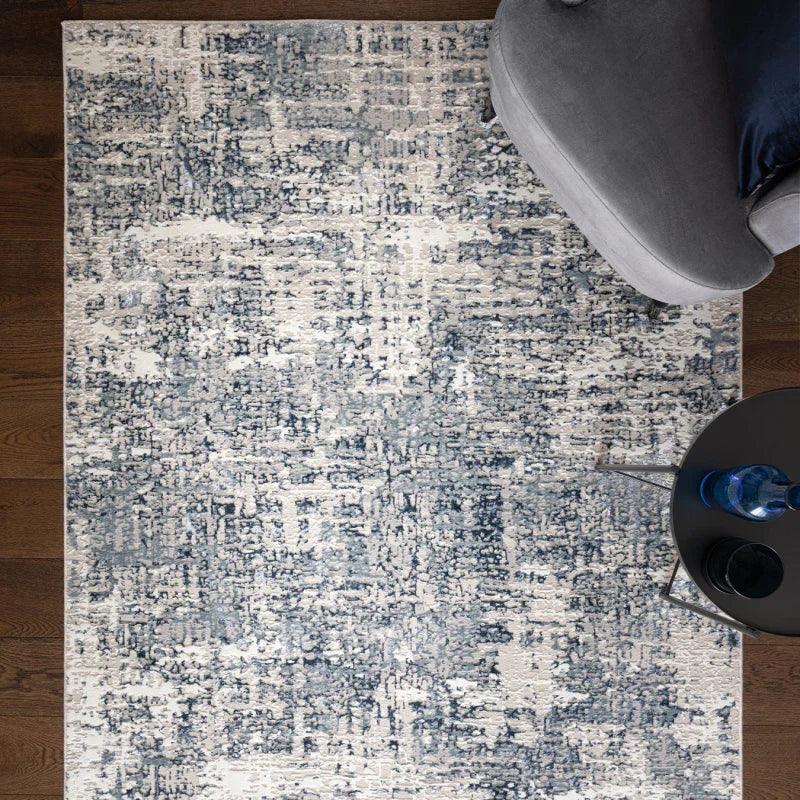 Blue and white abstract pattern rug on wooden floor beside grey sofa and round table