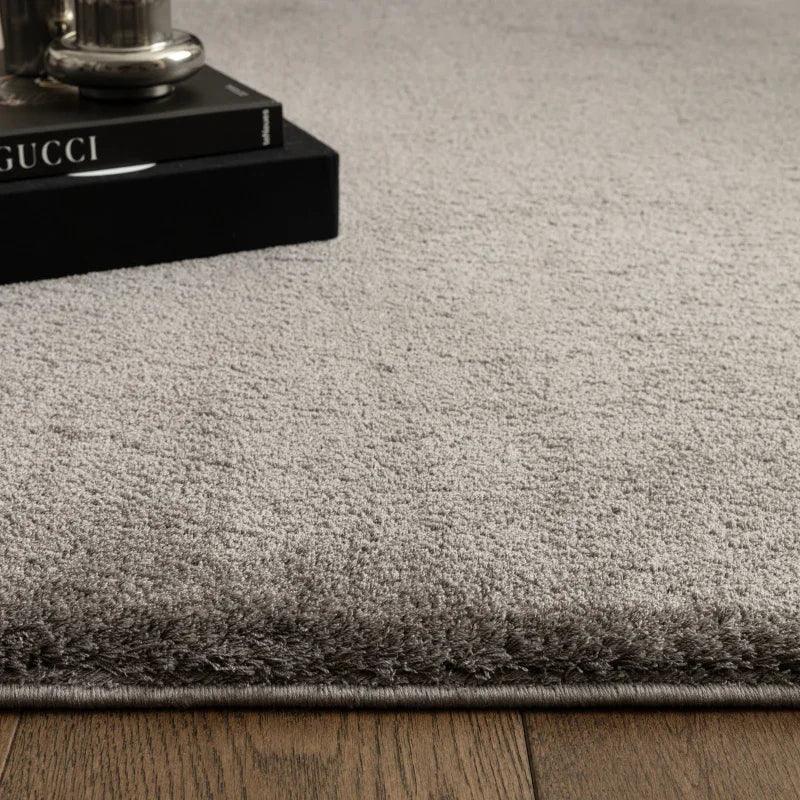 Grey plush area rug corner on wooden floor with books and lamp as decor