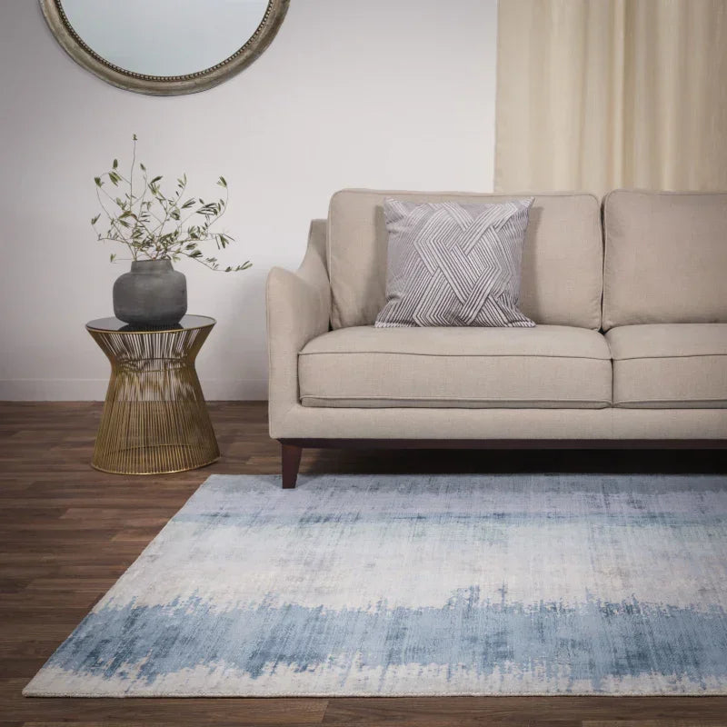 Beige fabric sofa with grey cushion, blue area rug, gold side table and vase in modern living room