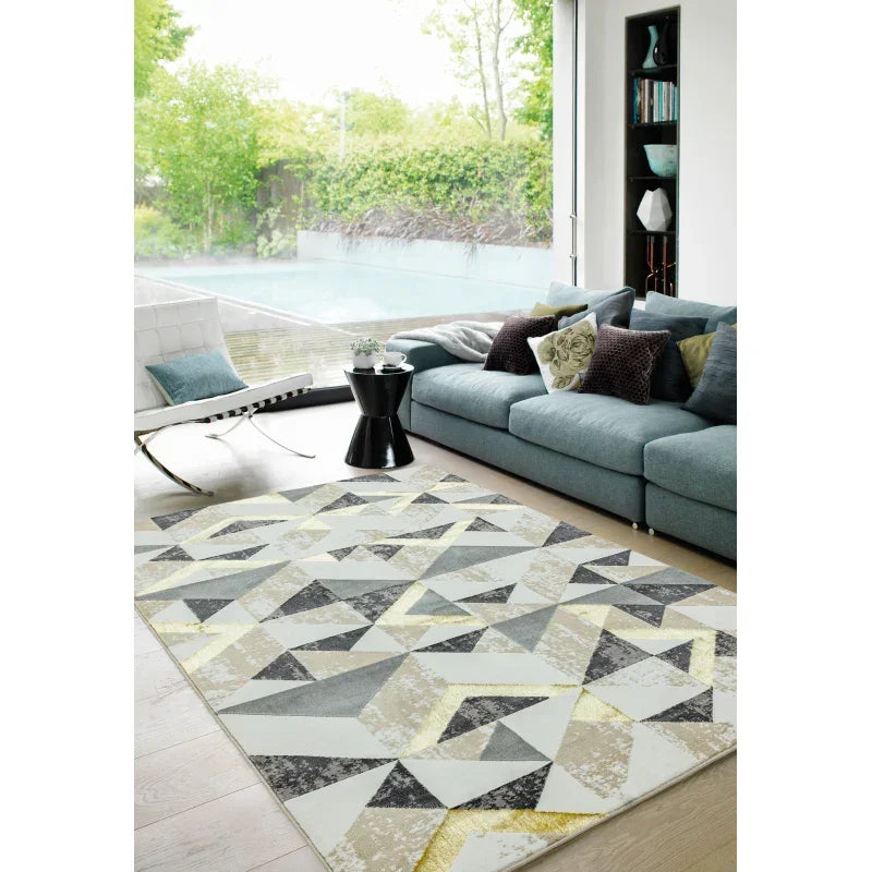 Modern geometric area rug in grey and yellow on wood floor beside blue corner sofa