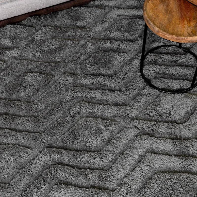 Grey geometric patterned rug with textured pile beside wooden table and sofa corner