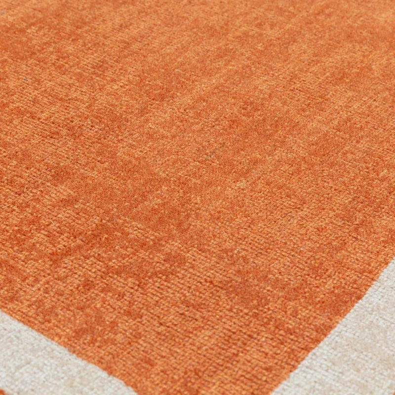 Close-up of orange textured rug with cream border corner detail