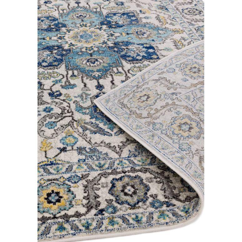 Blue and grey patterned area rug with floral motifs and visible corner fold