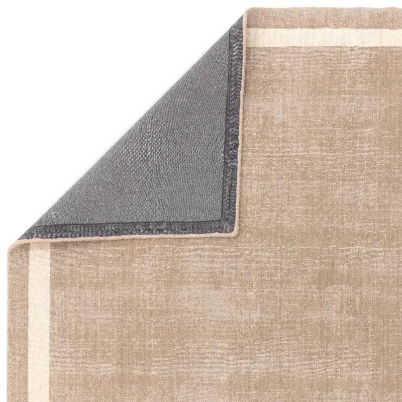 Beige bordered area rug with corner flipped, showing contrasting grey backing detail