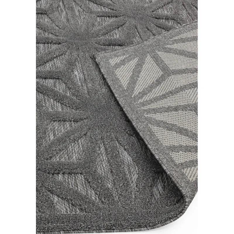 Grey textured rug with geometric leaf pattern and non-slip backing, close corner view
