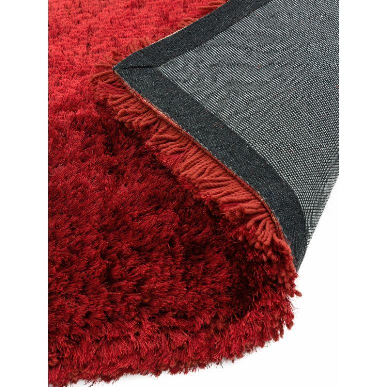 Red shaggy rug with fringe and non-slip backing, close-up of corner and texture