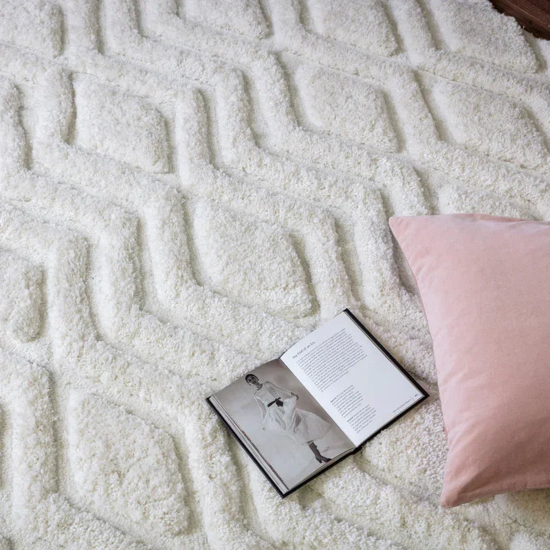 Ivory geometric textured rug with pink cushion and open book on soft pile surface