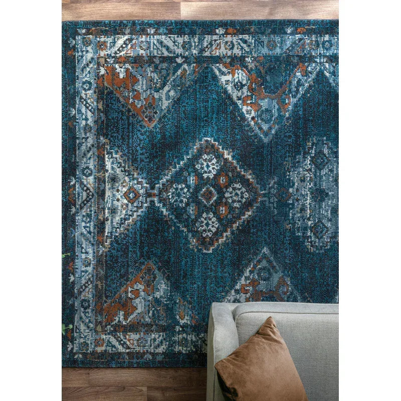 Blue patterned area rug with geometric motifs and a sofa corner on wooden floor