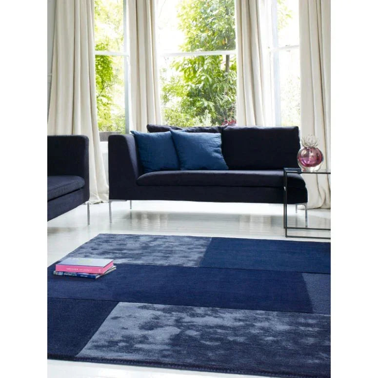 Navy blue fabric sofa with blue cushions beside glass side table in a bright living room