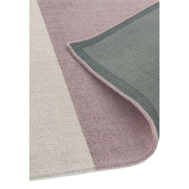 Close-up of striped area rug with pink, cream, and grey tones, corner folded to show backing