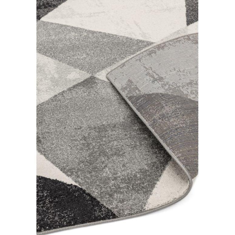Grey geometric area rug with modern pattern and visible corner fold showing backing