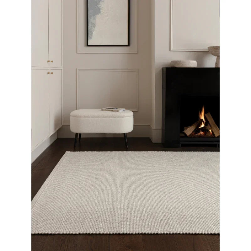 Cream wool rug on dark wood floor beside ottoman and lit fireplace in modern living room
