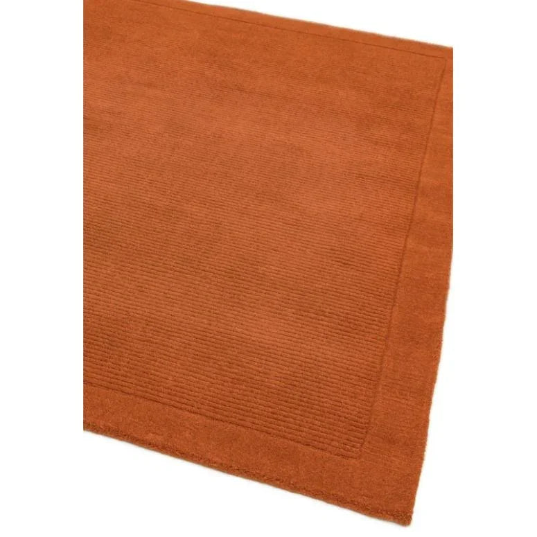 Burnt orange wool rug with subtle textured border, corner angle view