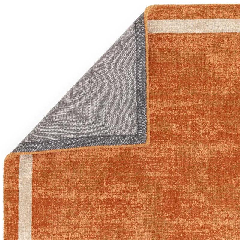 Burnt orange area rug with corner turned to show grey backing and beige border detail
