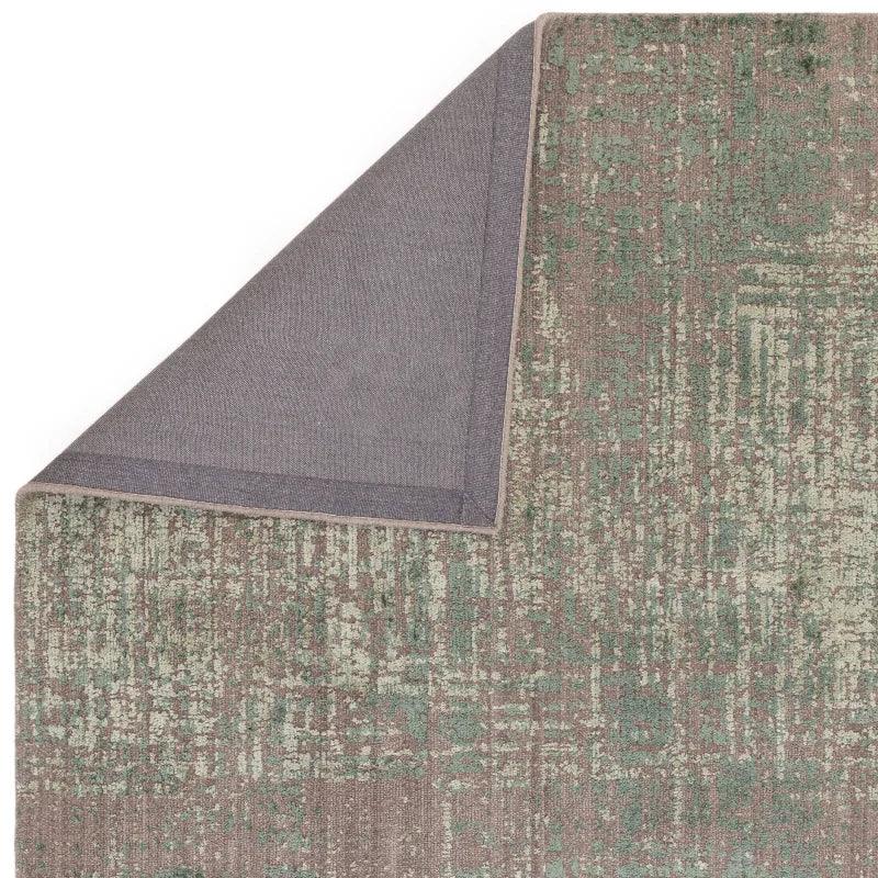 Green and beige patterned area rug with corner folded to show backing