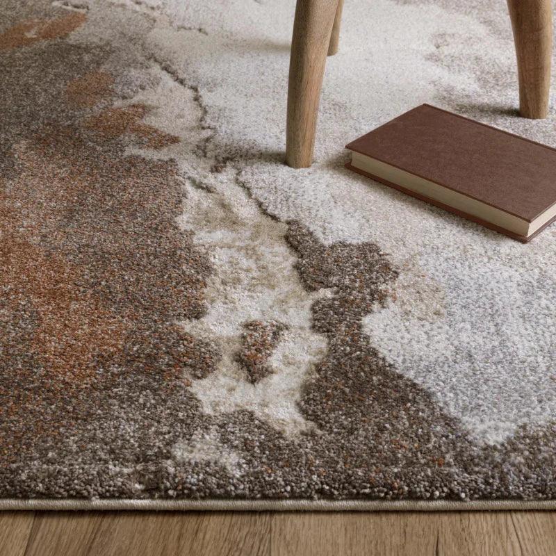 Abstract patterned area rug with brown, beige, and cream tones on wooden floor