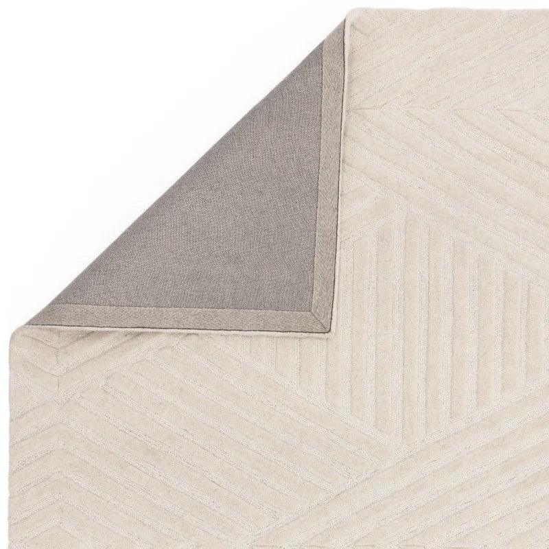 Beige patterned rug with textured geometric design and grey fabric backing corner exposed