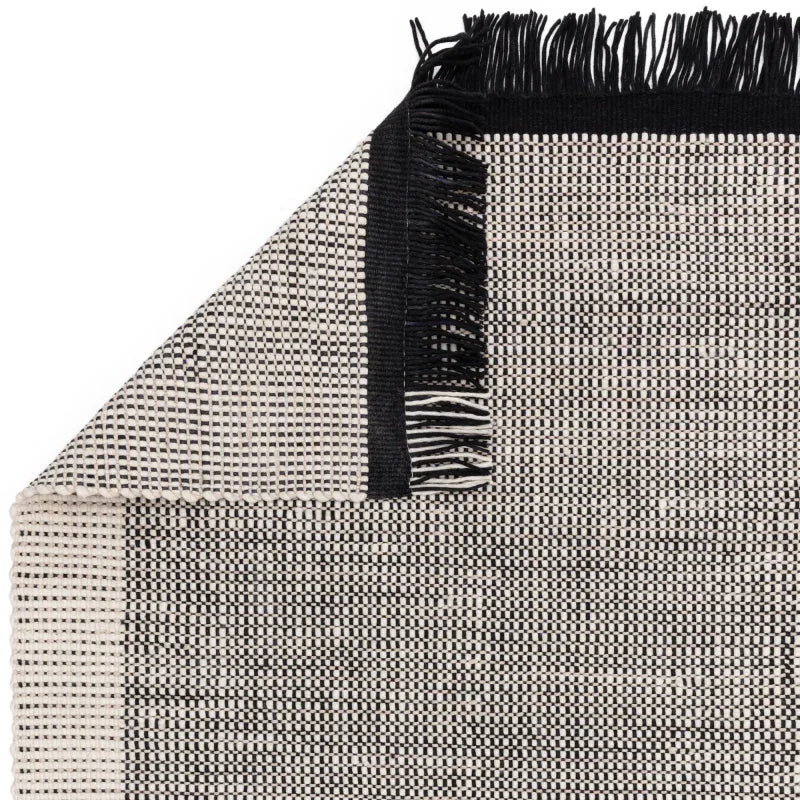 Black and cream woven rug with fringed edge, close up showing texture and corner fold