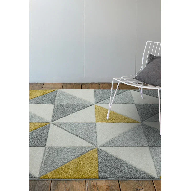 Geometric area rug with grey and yellow triangles on wooden floor beside white chair