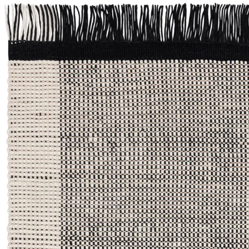 Black and cream woven rug corner with black fringe detail and geometric pattern