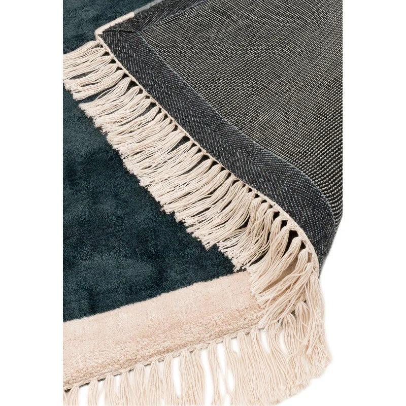 Closeup of woven rug with black and cream fringe corner detail on soft textured surface
