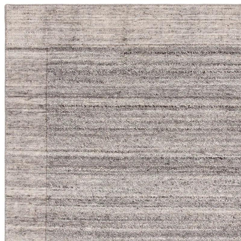 Grey textured area rug corner with subtle stripe pattern and woven border detail