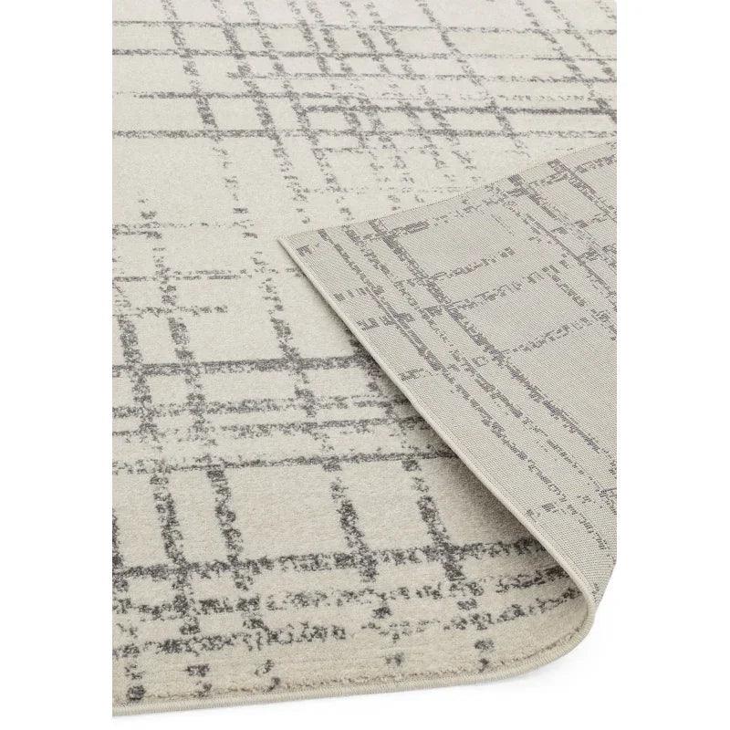 Modern area rug with grey geometric grid pattern and folded corner on cream background