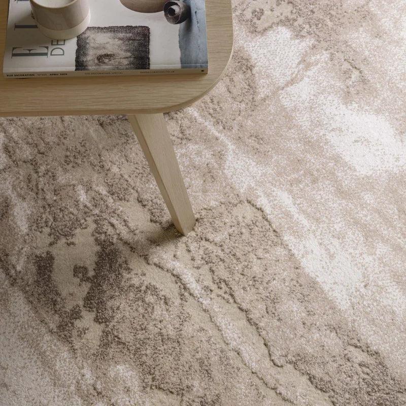 Beige abstract rug with thick pile beneath light wood coffee table and magazine