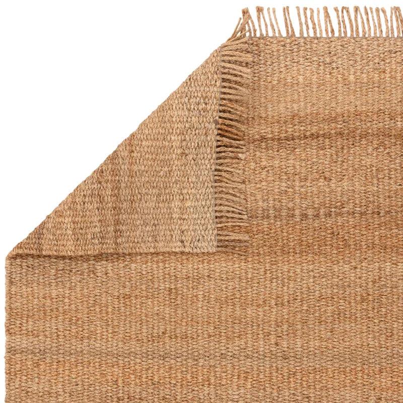 Natural jute rug with woven texture and fringe detail, corner folded to show thickness