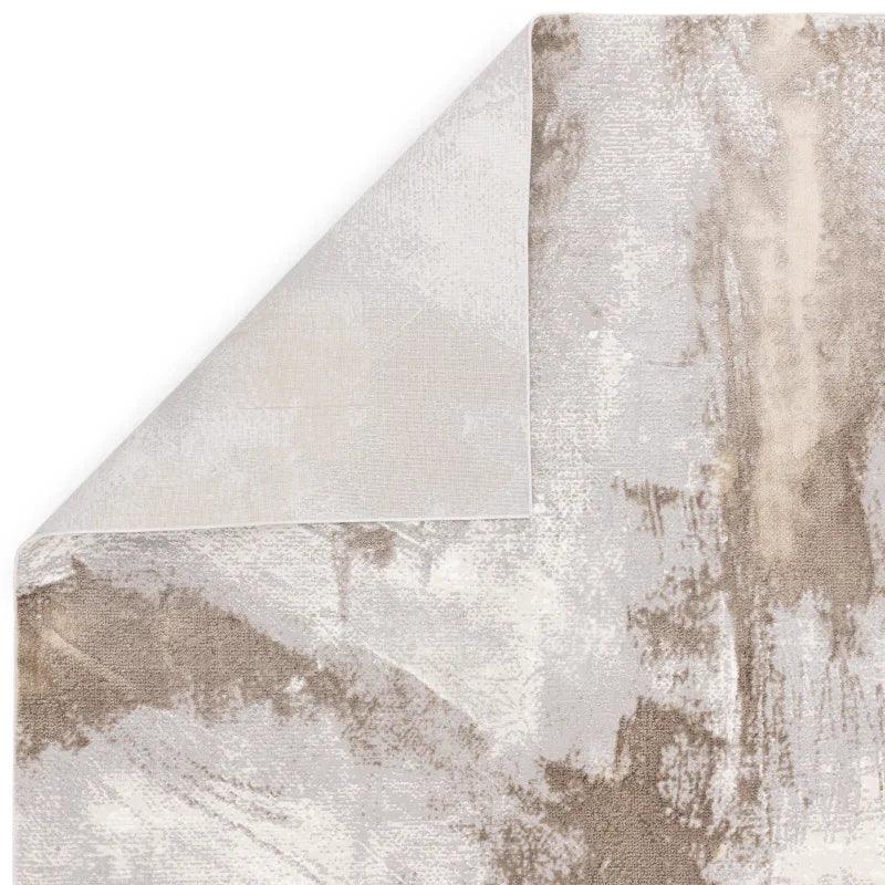 Closeup of abstract beige and grey area rug with corner flipped to show backing