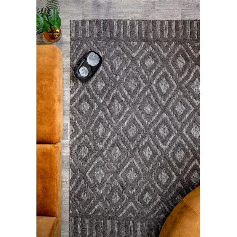 Grey diamond patterned rug on wooden floor beside orange sofa and plant