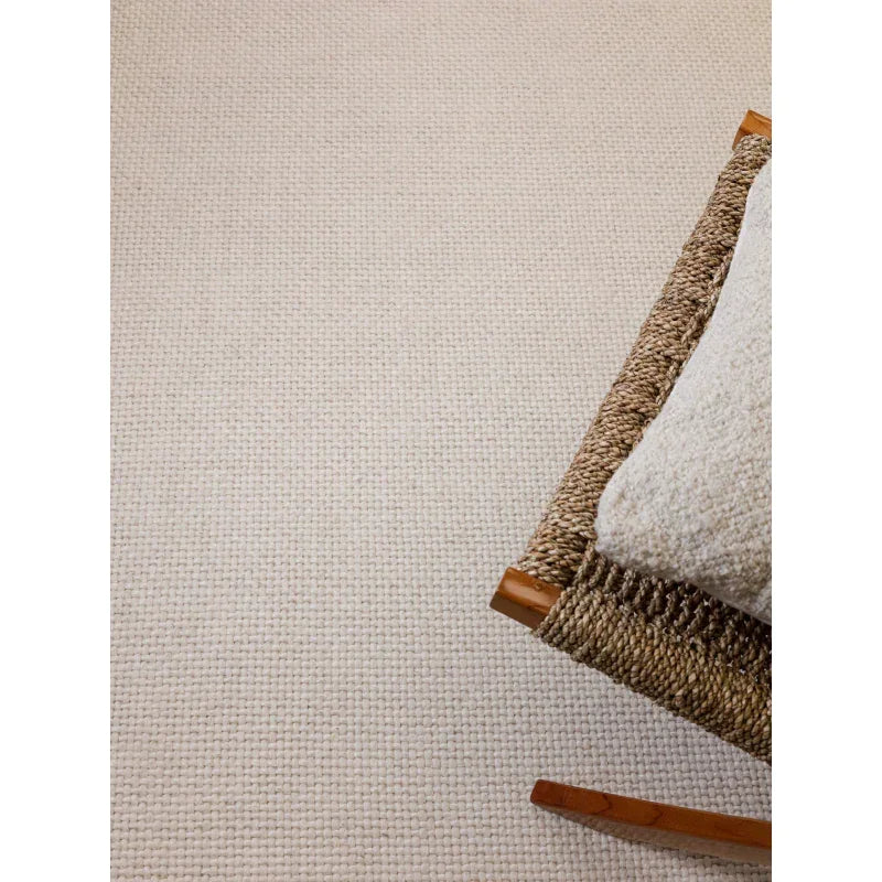 Closeup of beige woven rug next to a wooden and rattan chair with textured cushion