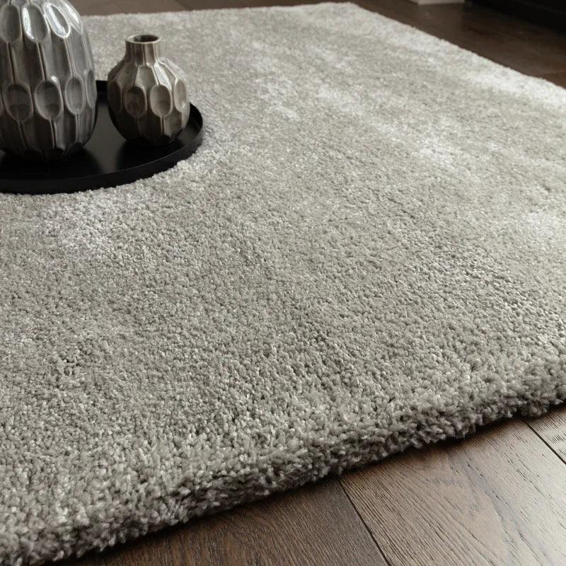 Light grey shaggy rug on wooden floor with ceramic vases on black tray