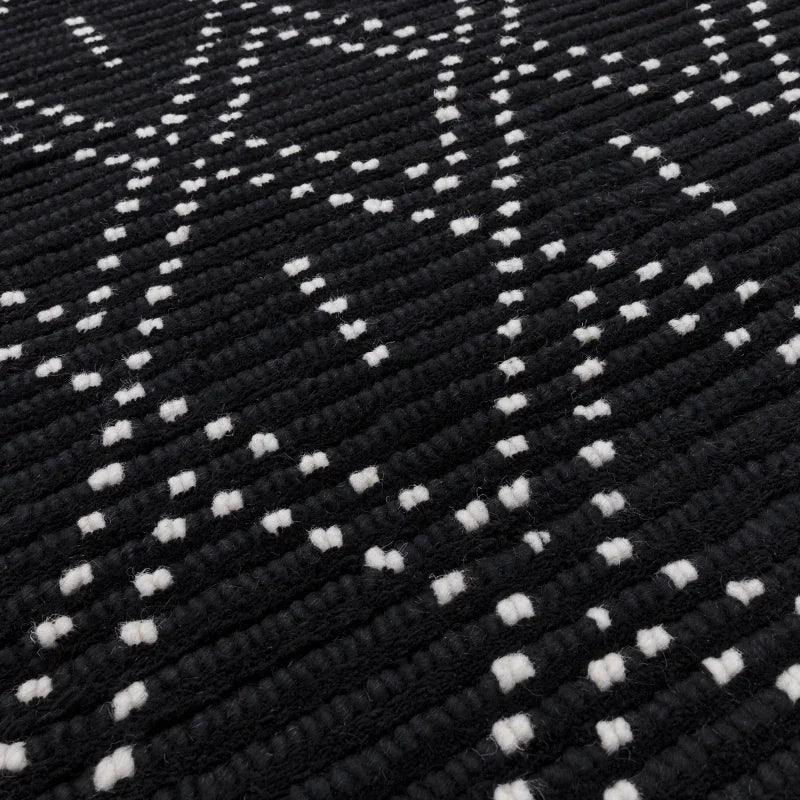 Black textured rug with white geometric pattern, close-up of woven wool detail