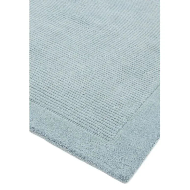Light blue textured rug with ribbed pattern and solid border, corner detail view