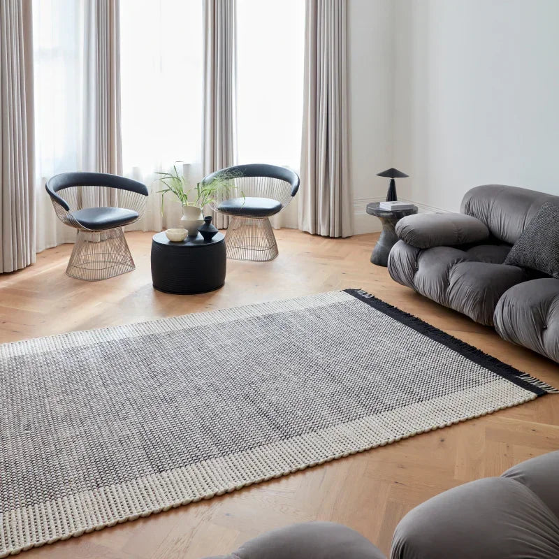 Modern living room with grey sofa, two accent chairs, monochrome rug and wood flooring